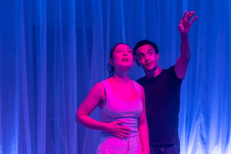 Performers Miles Barrow and Harriet Gordon-Anderson stand together, looking upwards in the direction of Miles' arm pointing up