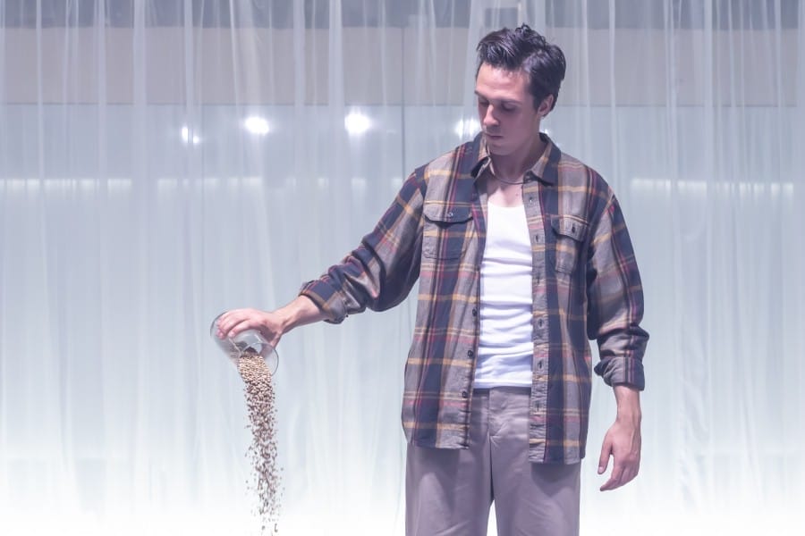 Performer Ziggy Heath pours lentils from a jar onto the floor