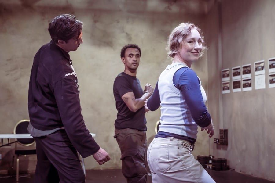 A woman and a man dancing, with a third person standing to their left, behind them.